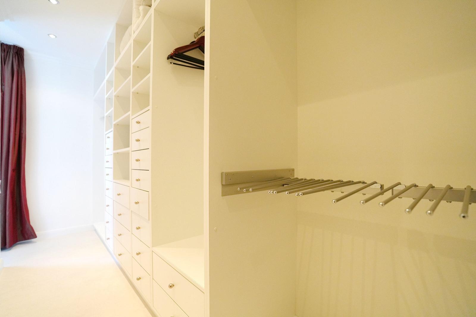 Großer Kleiderschrank mit Schubladen und Kleiderständer. Roter Vorhang im Hintergrund.