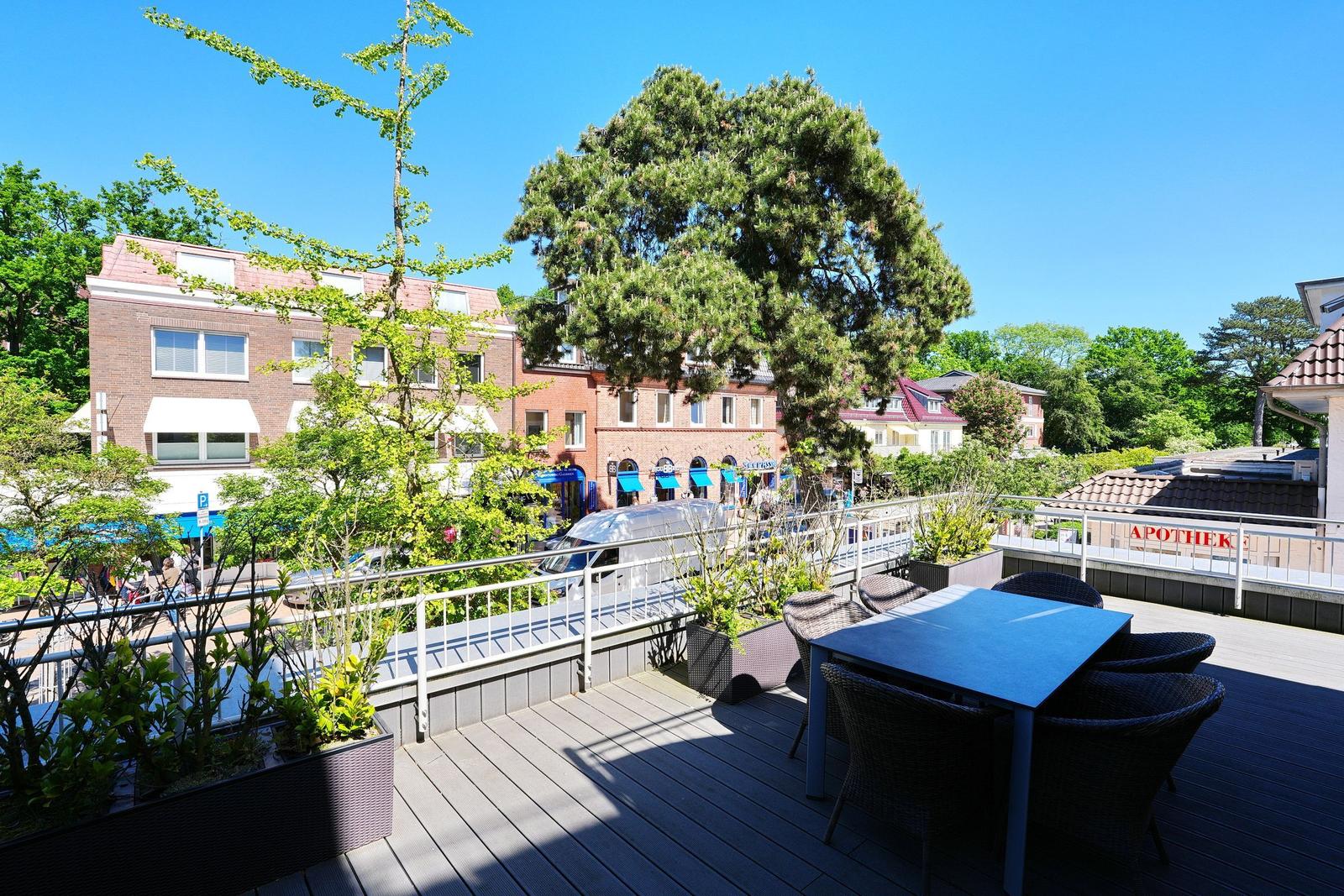 Terrasse mit Tisch und Stühlen, Blick auf Gebäude und Bäume.