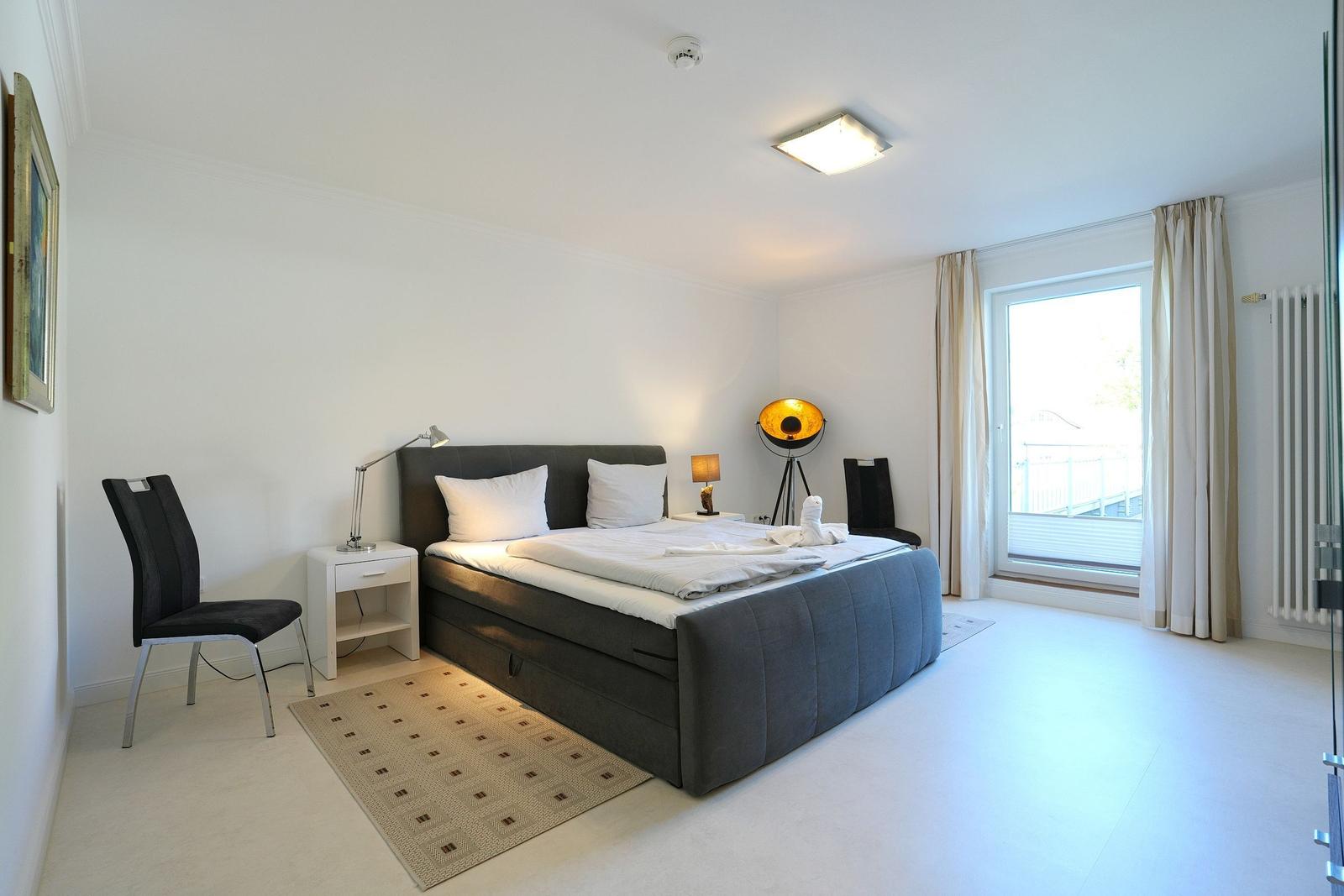 Schlafzimmer mit Bett, Nachttisch, Stuhl und Fenster.