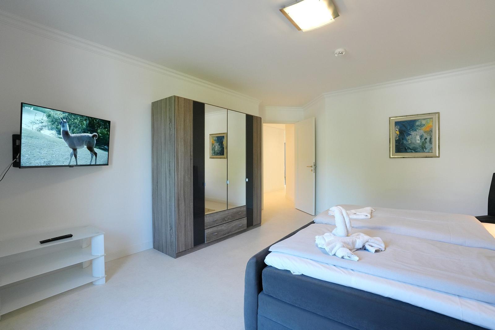 Schlafzimmer mit Doppelbett, Kleiderschrank und Wand-TV.