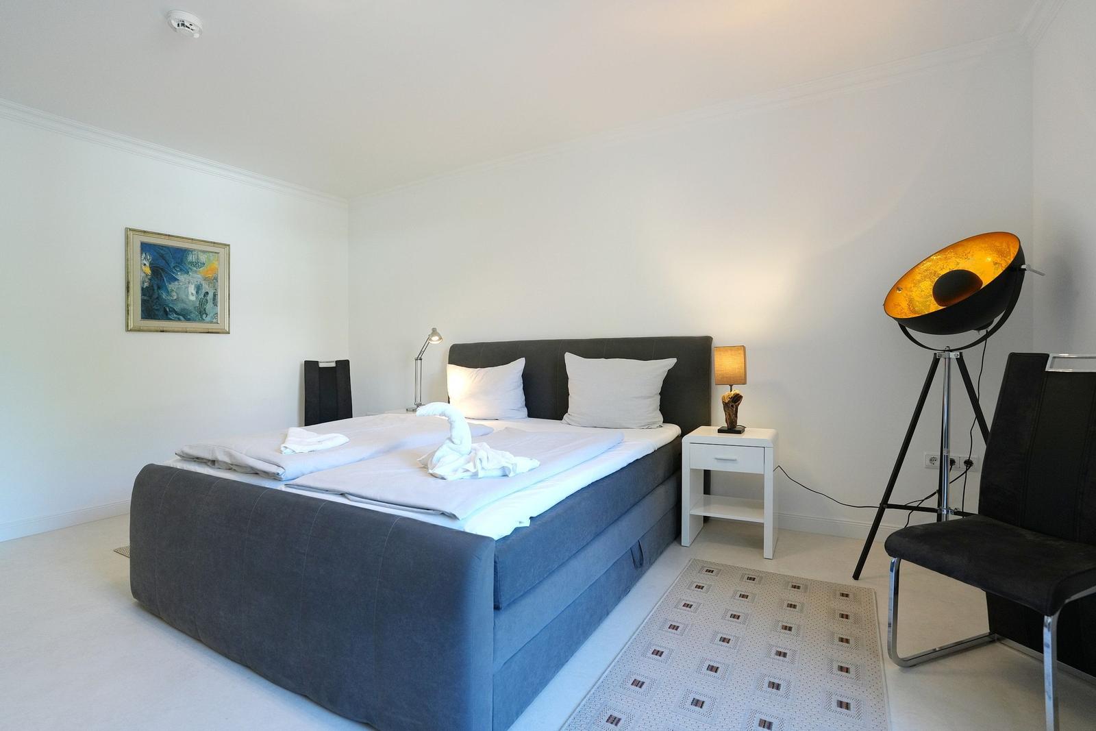 Schlafzimmer mit Bett, Nachttisch, Stehlampe und Wandbild.