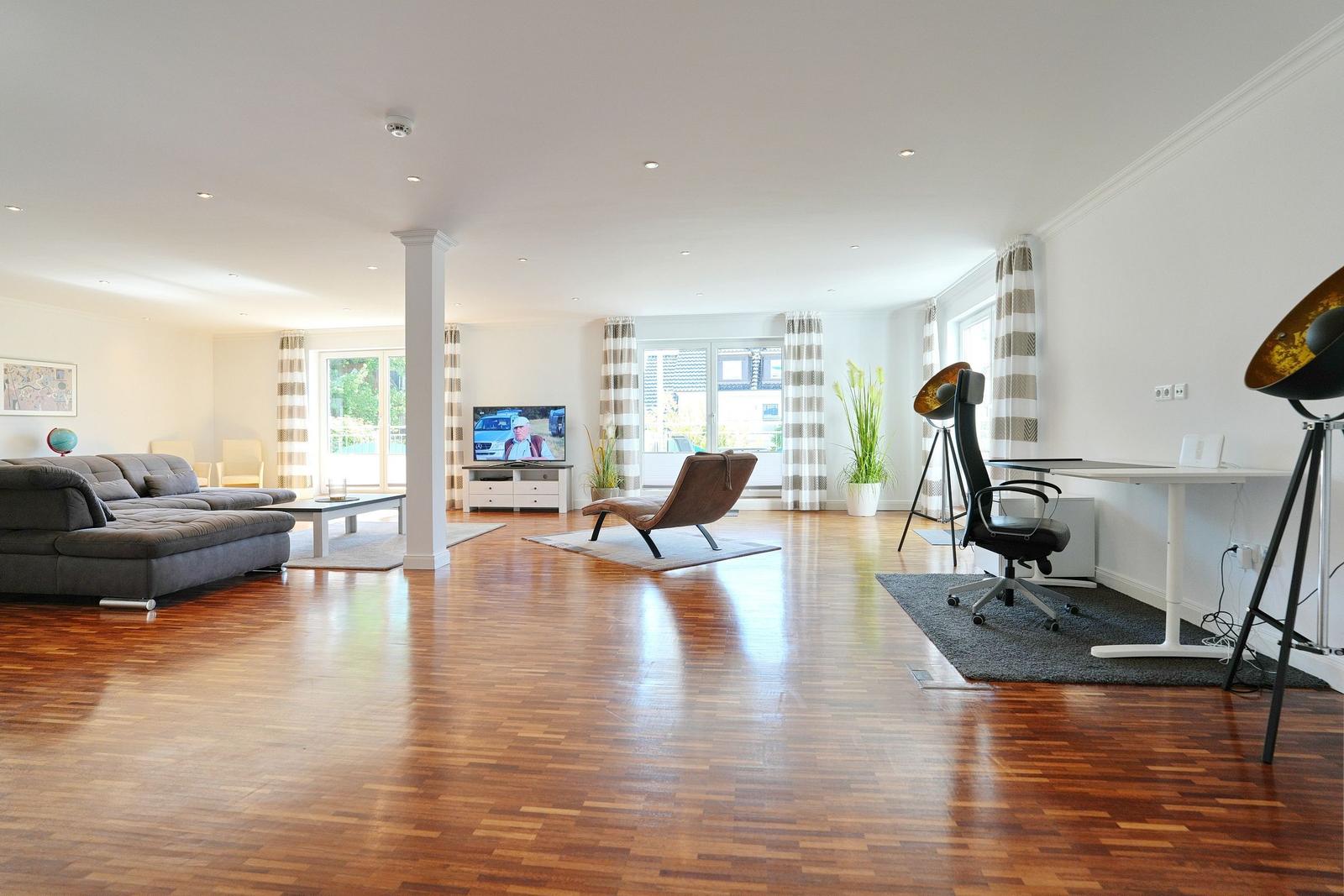 Wohnzimmer mit Sofa, Fernseher und Schreibtisch auf Holzboden.