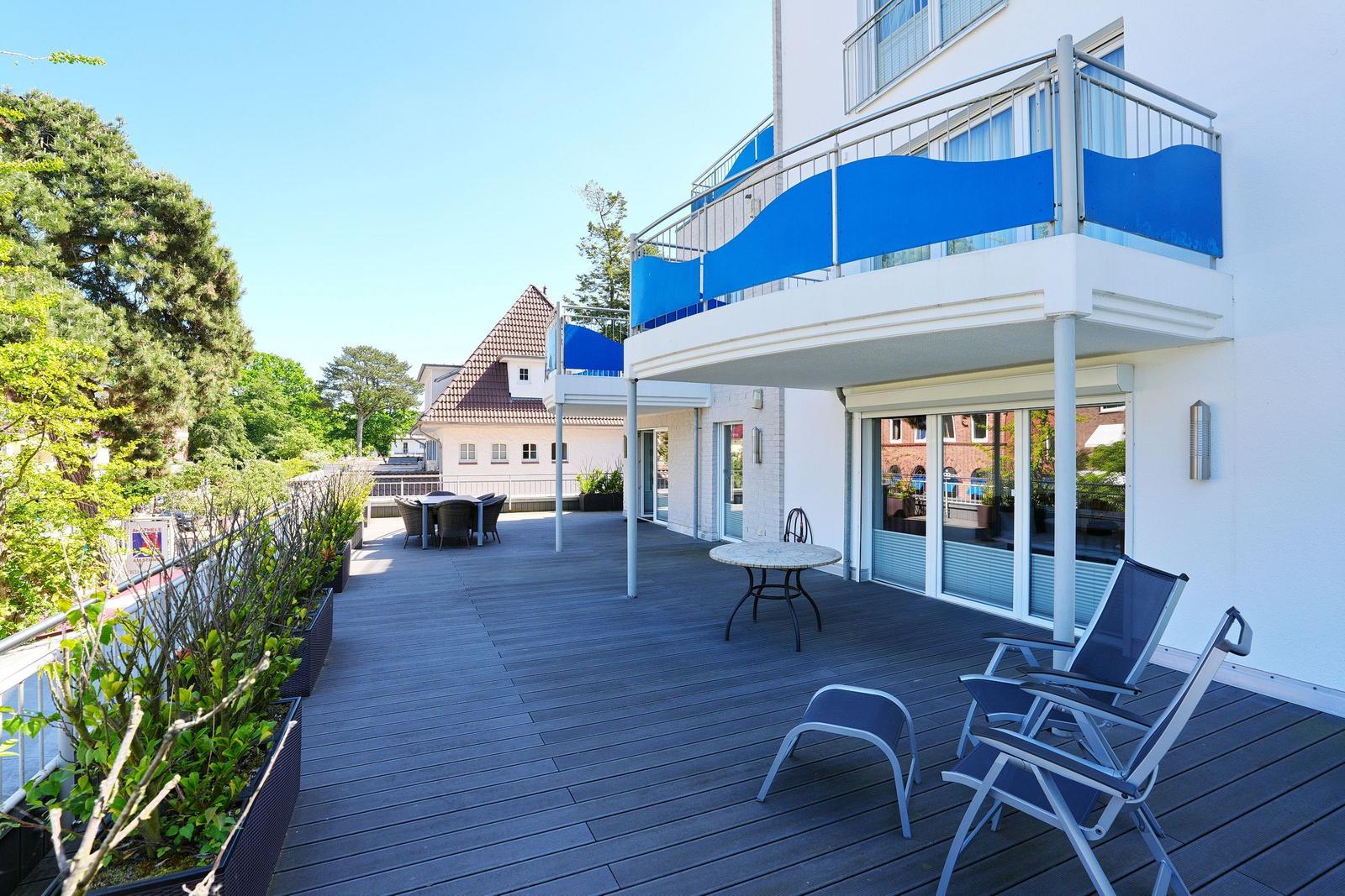 Terrasse mit Liegestühlen, Tisch und Pflanzen. Hochparterre mit blauem Sonnenschutz.