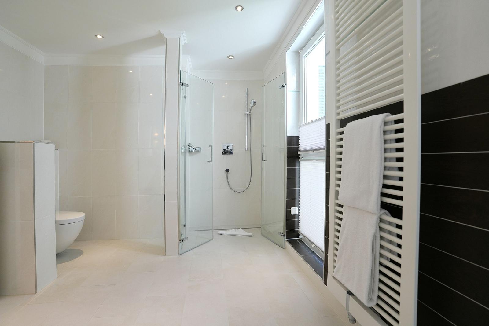 Badezimmer mit Dusche, Toilette und Heizkörper. Fenster mit Jalousie.