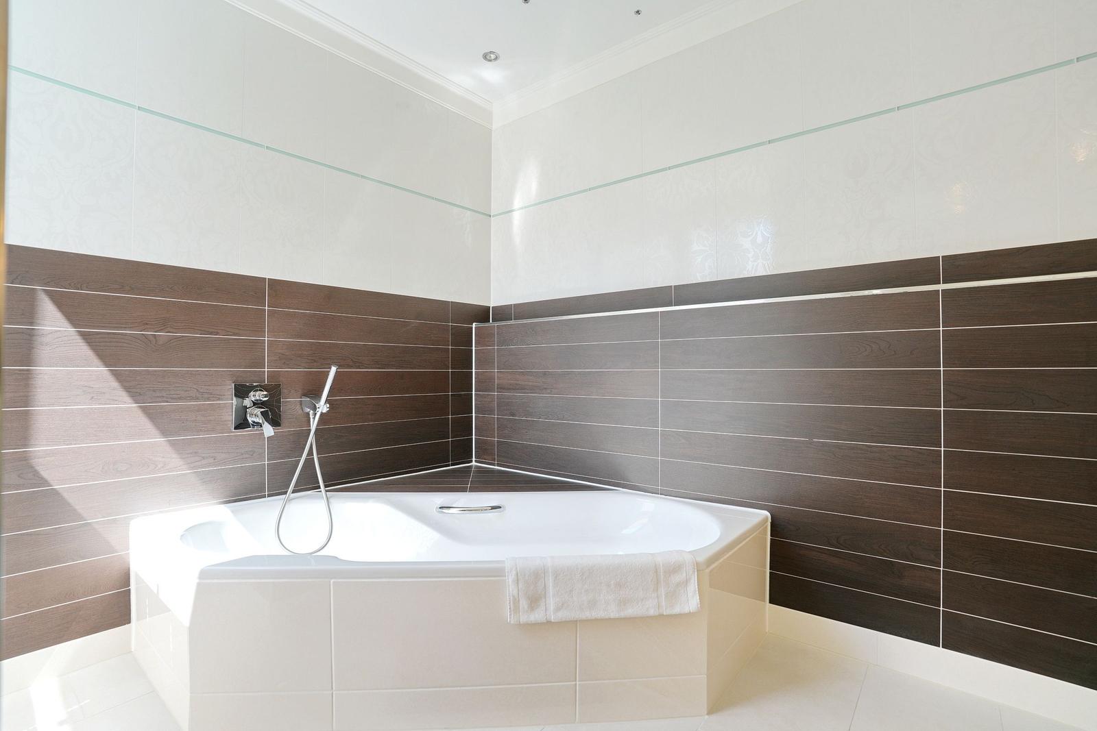 Eckbadewanne mit Duschbrause und Holzfliesen an den Wänden.