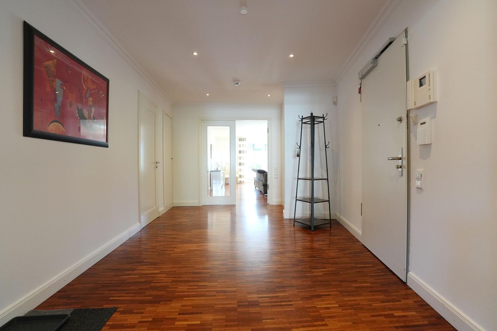 Flur mit Holzboden, Wandbild und Garderobe. Tür zum Wohnzimmer sichtbar.