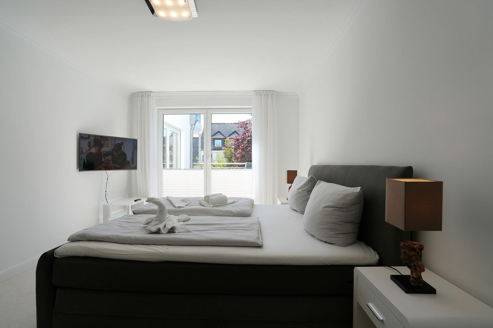 Schlafzimmer mit Doppelbett, Fernseher und Balkonansicht.