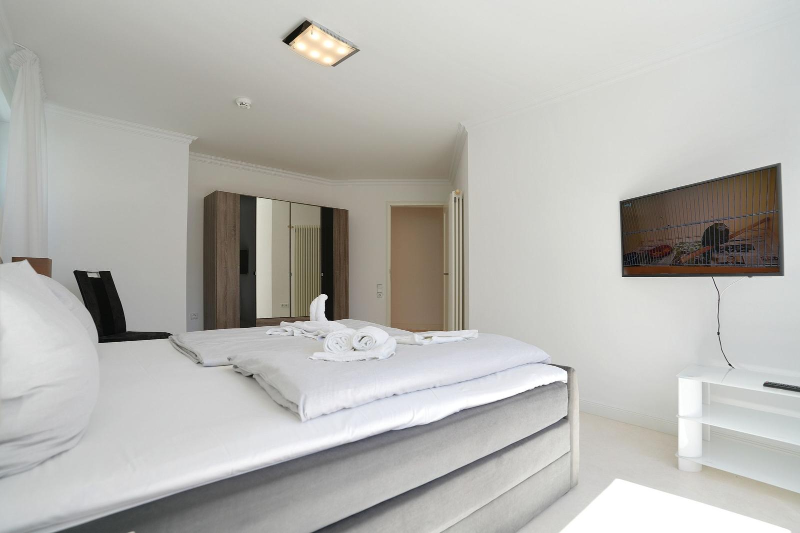 Schlafzimmer mit Bett, Kleiderschrank und Fernseher an der Wand.