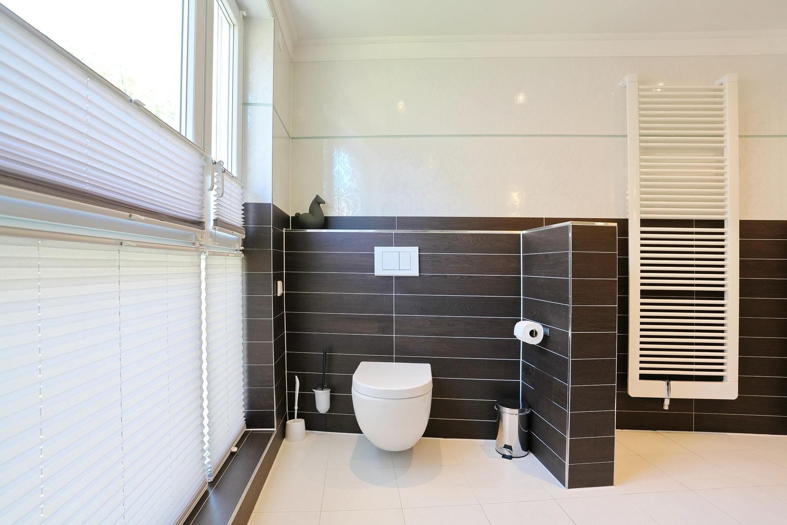 Badezimmer mit Toilette, Heizkörper und Fenster mit Jalousien.