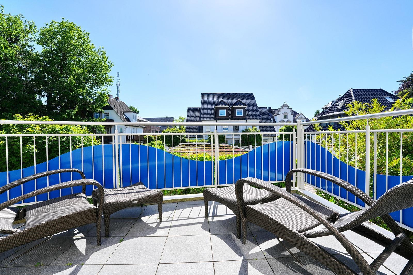 Terrasse mit Liegestühlen und Blick auf Häuser und Bäume.