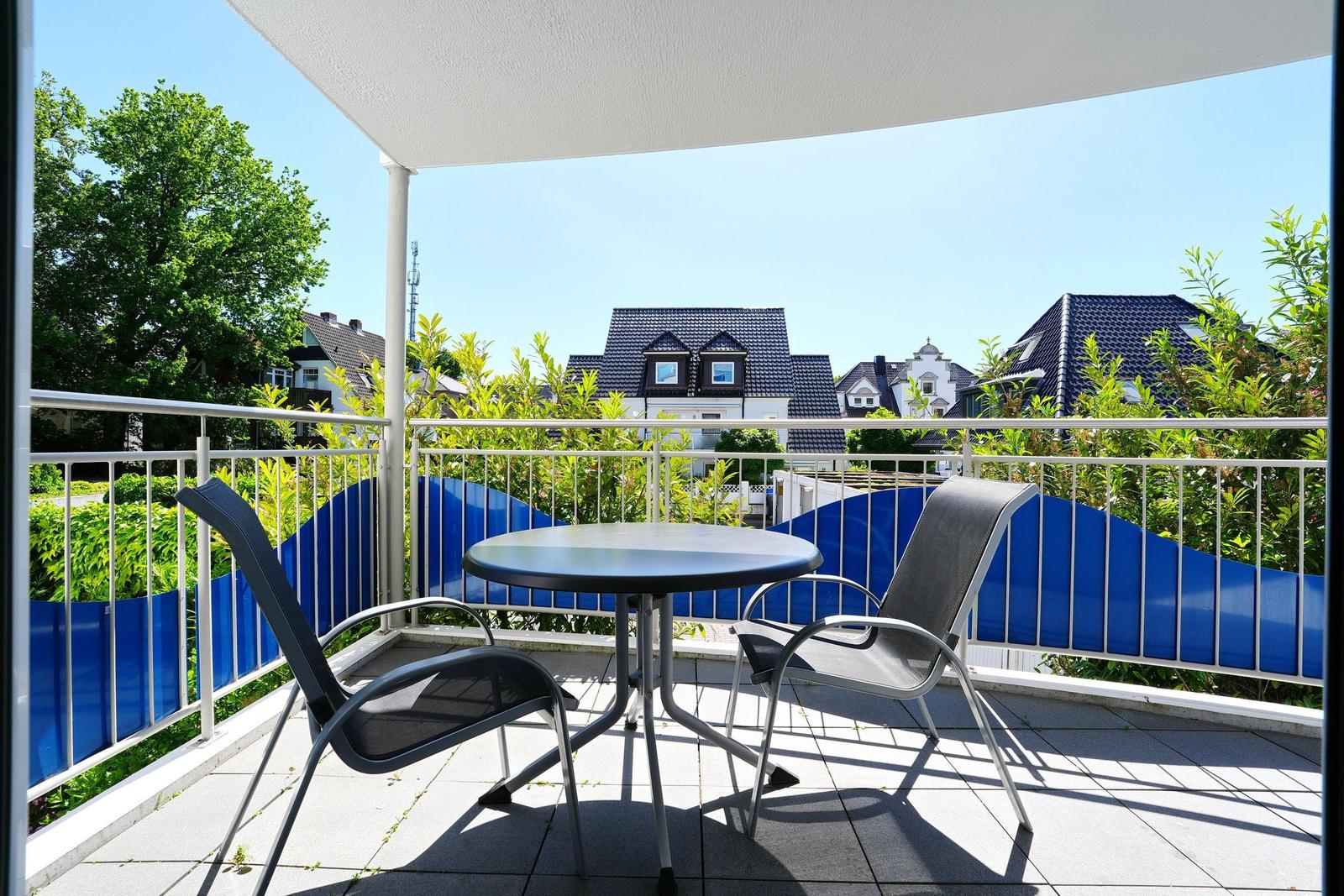 Terrasse mit Tisch und zwei Stühlen, Blick auf Häuser und Grünflächen.