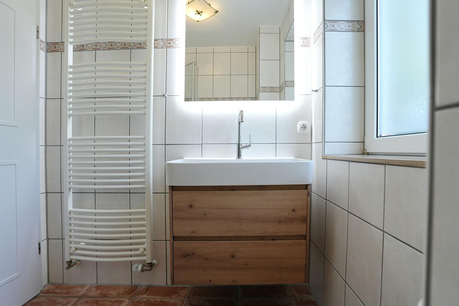 Badezimmer mit Waschbecken, Spiegel, Heizkörper und Fenster