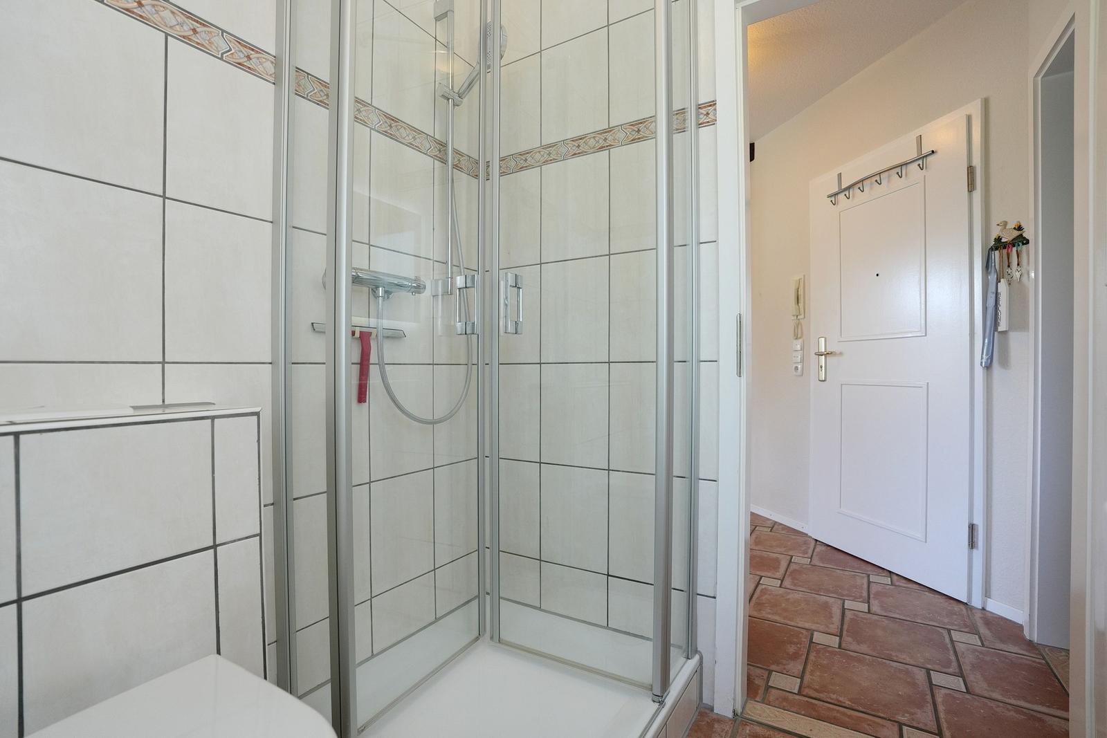 Bad mit Dusche und Fliesenboden. Tür führt in den Flur.
