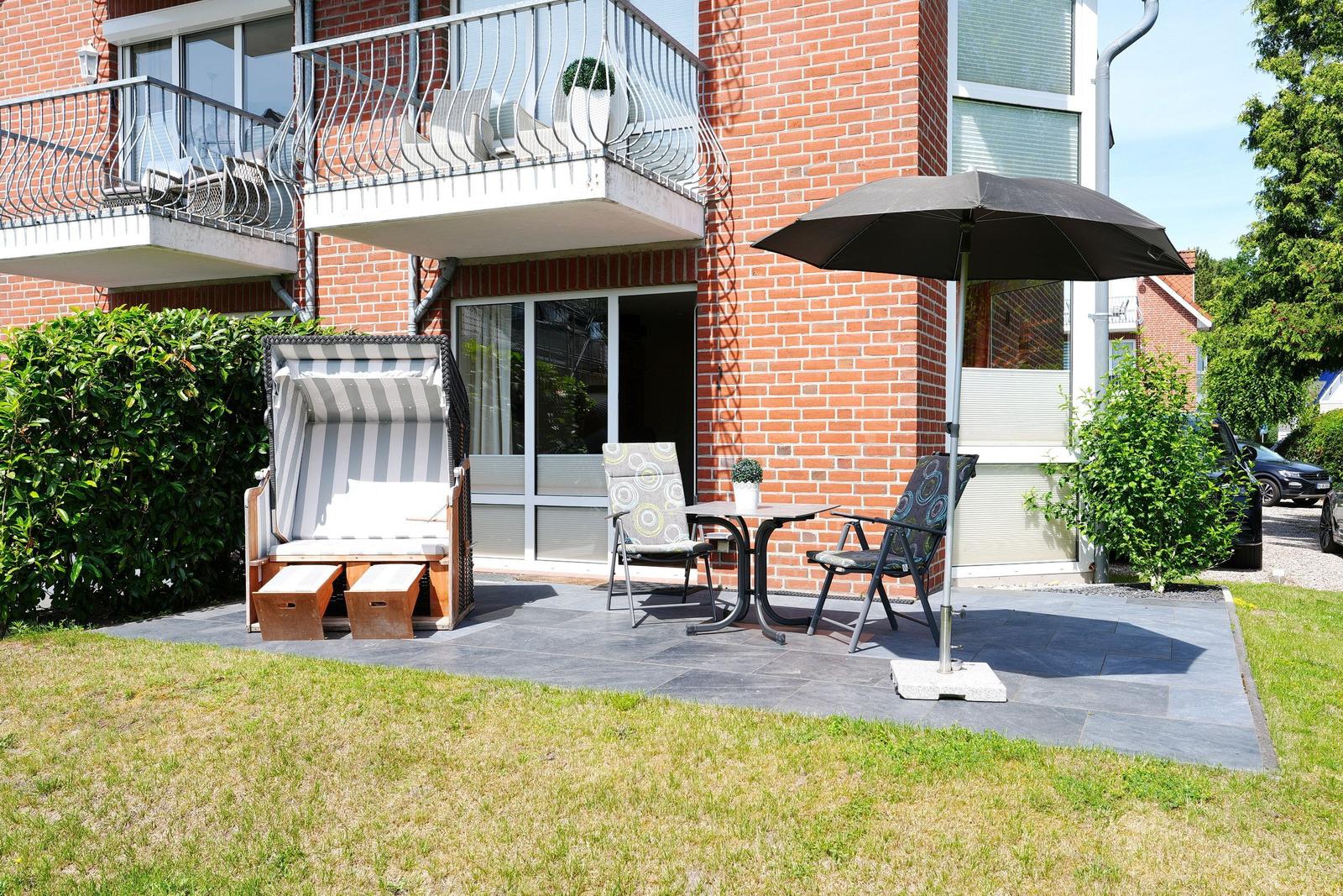 Terrasse mit Liegestuhl, Tisch, zwei Stühlen und Sonnenschirm vor rotem Backsteinhaus.