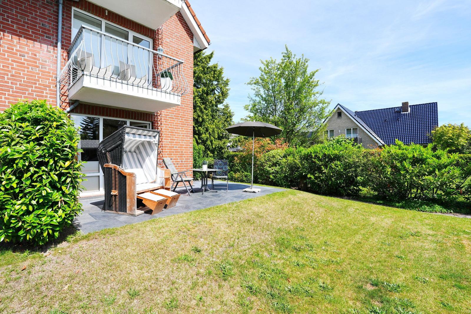 Hinterhof mit Liegestuhl, Tisch, Stühlen und Sonnenschirm. Roter Backsteinbau mit Balkon.