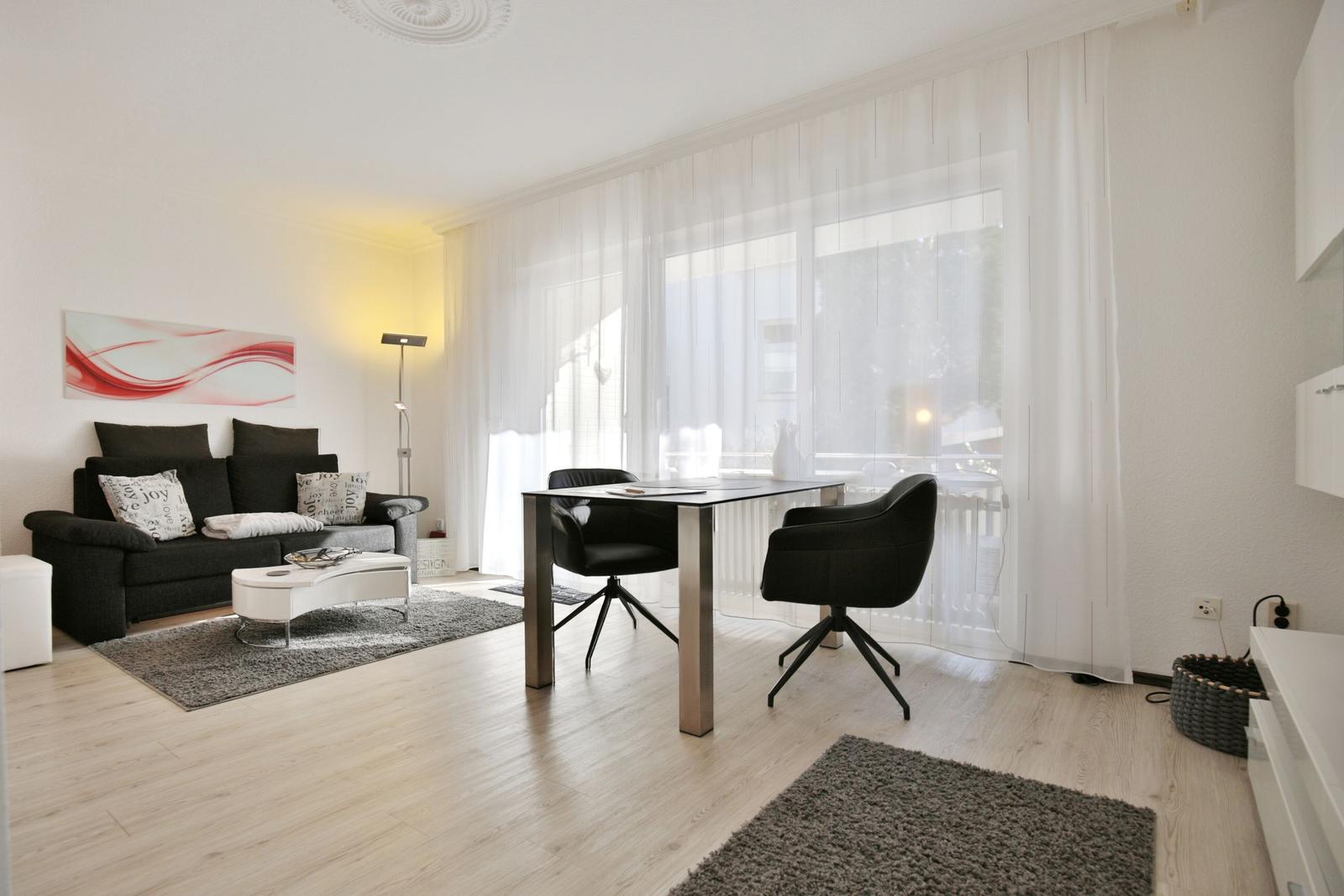 Wohnzimmer mit Sofa, Esstisch und Fenster mit weißen Vorhängen.