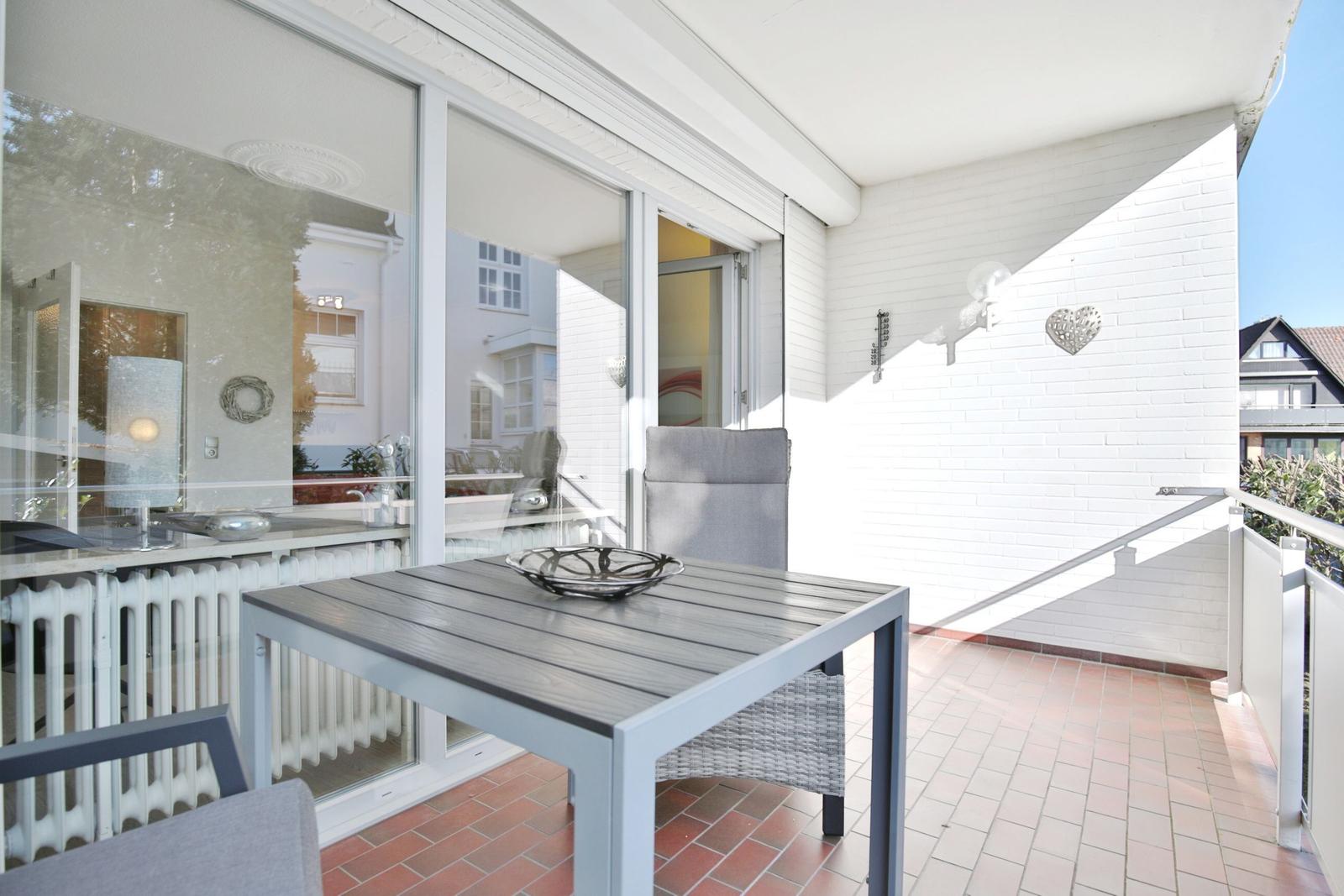 Terrasse mit Tisch, Stühlen und Blick ins Haus. Weiße Wand und Geländer.