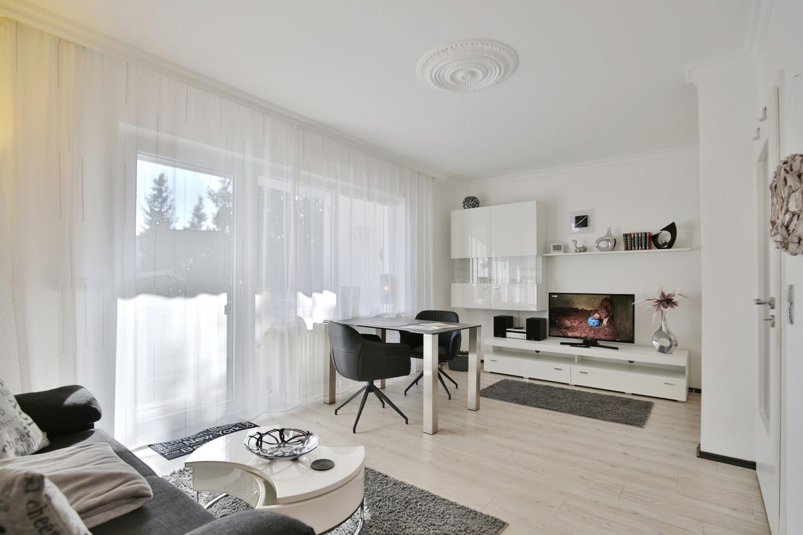 Wohnzimmer mit Essbereich, TV und großem Fenster mit weißen Vorhängen.