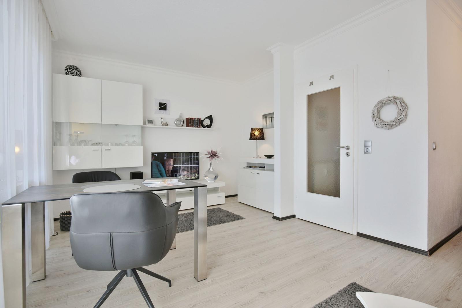 Ein Raum mit Esstisch, TV und weißen Schränken. Tür mit Glas und Wanddekoration.