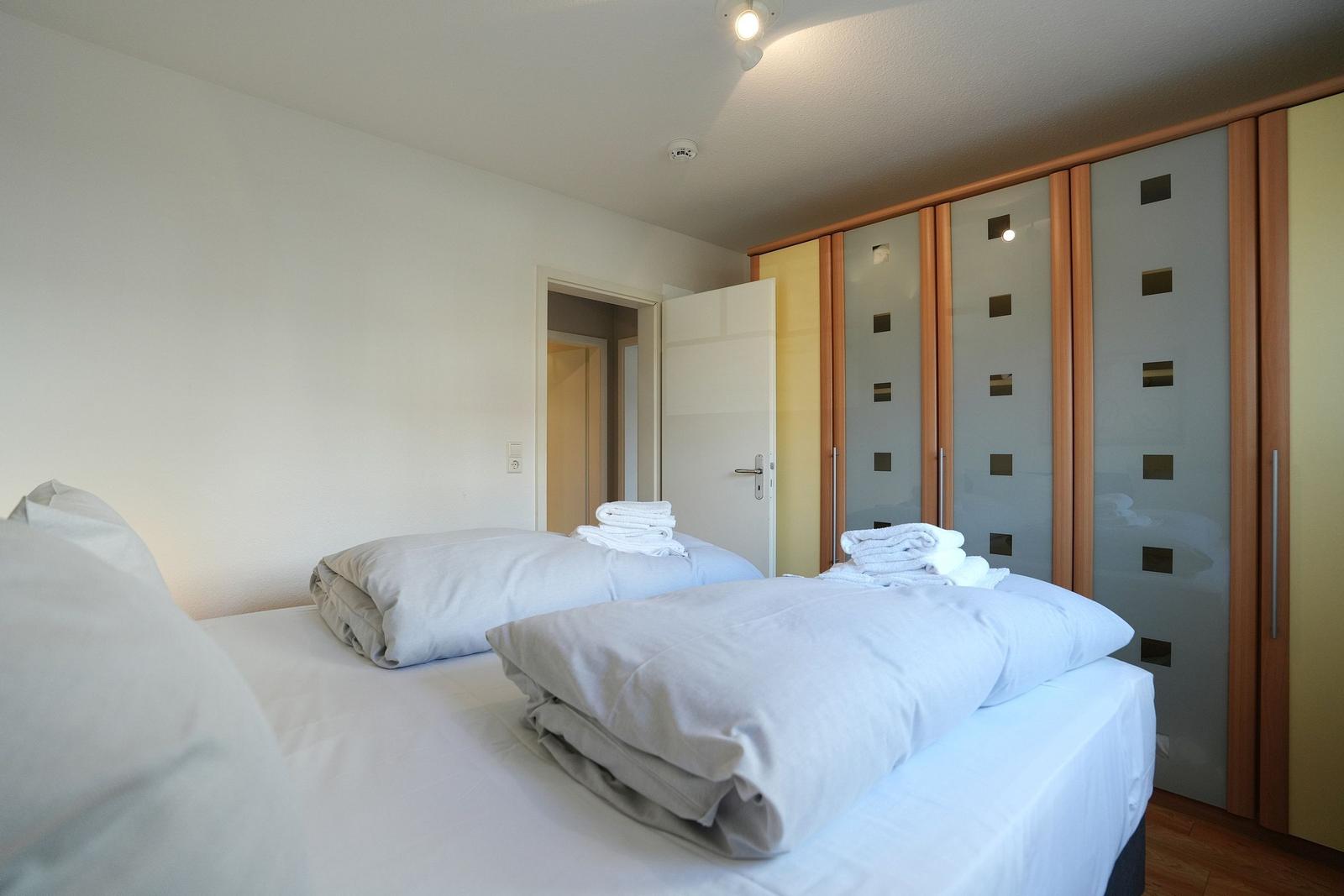 Schlafzimmer mit Doppelbett, gefalteten Bettwäsche und Glaswand-Schrank.