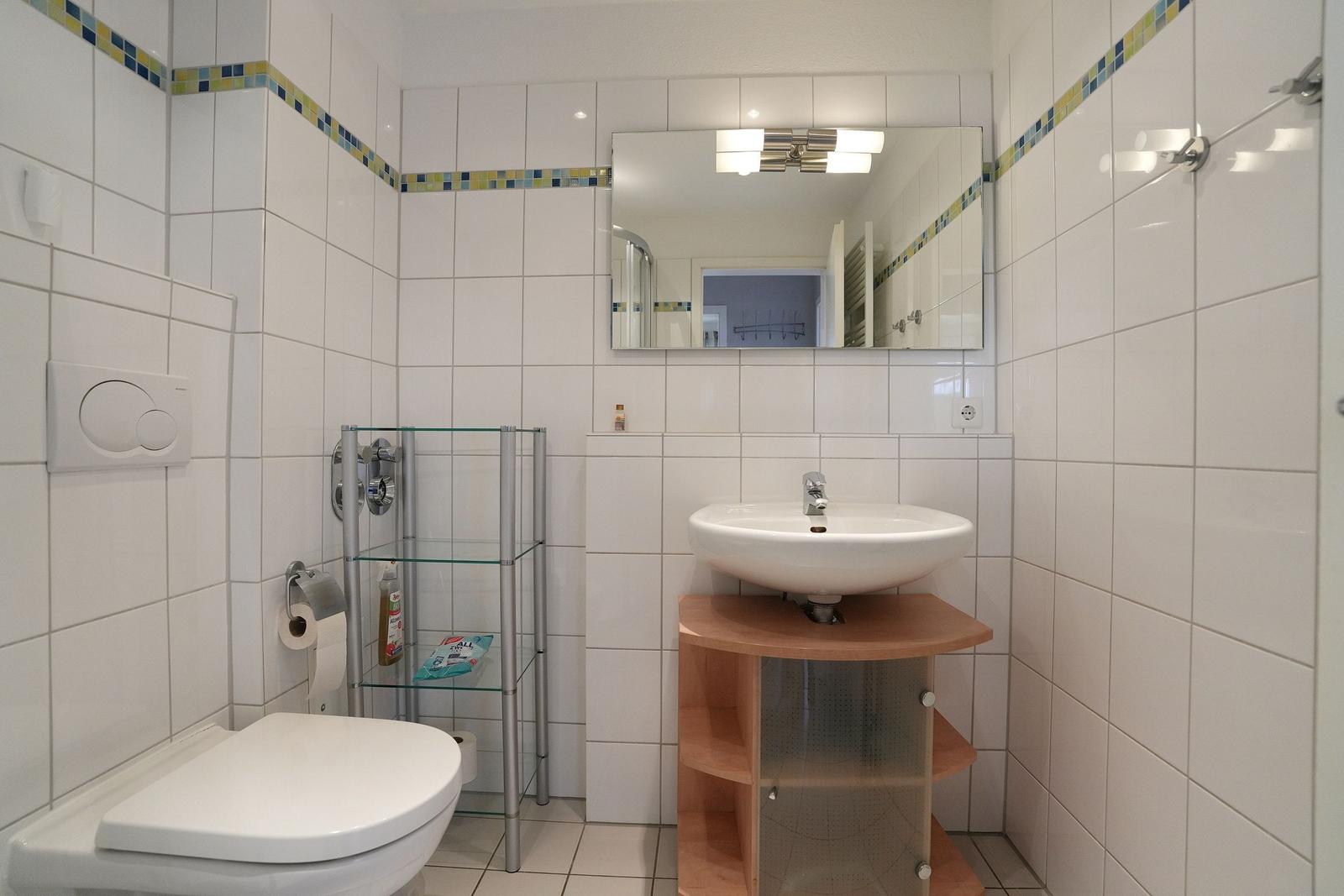 Badezimmer mit Toilette, Waschbecken und Spiegel. Wandfliesen mit farbiger Bordüre.