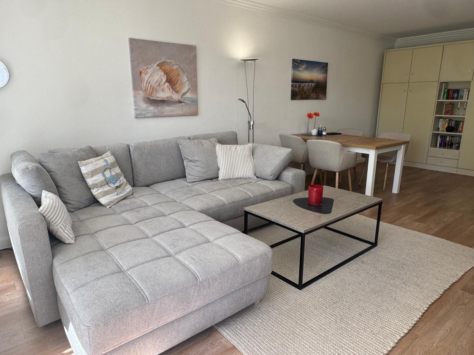 Großer Wohnbereich mit grauem Sofa, Esstisch und Bücherregal.