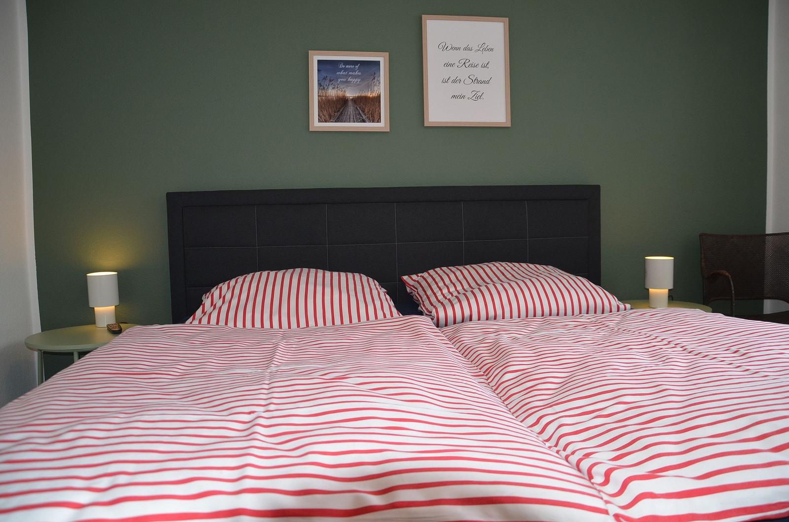 Doppelbett mit rot-weiß gestreifter Bettwäsche, dunkelgrüne Wand, zwei Nachttische mit Lampen und zwei Bilder.