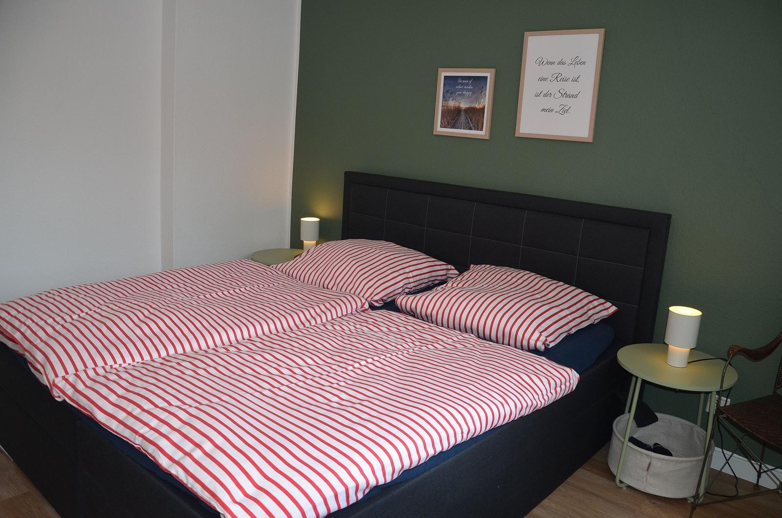 Schlafzimmer mit Bett, Nachttischen und Wandbildern.