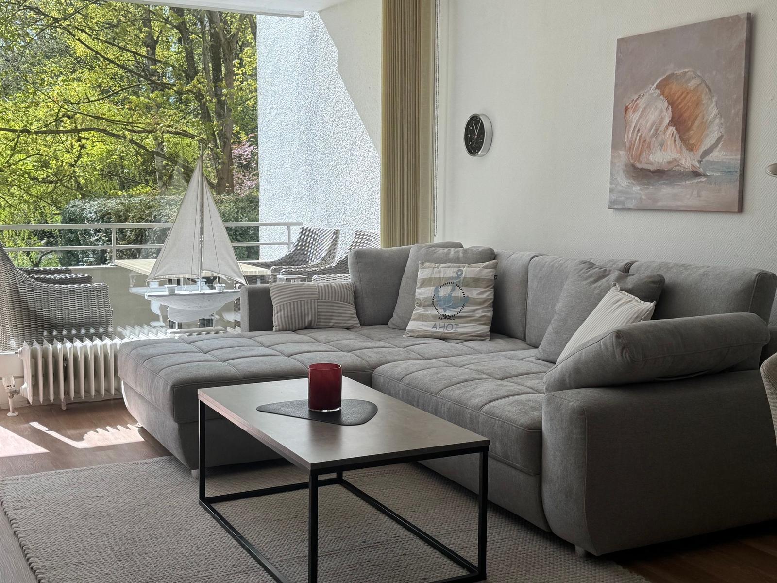 Ein grauer Sofa-Bereich mit Tisch und Blick auf Balkon mit Garten.