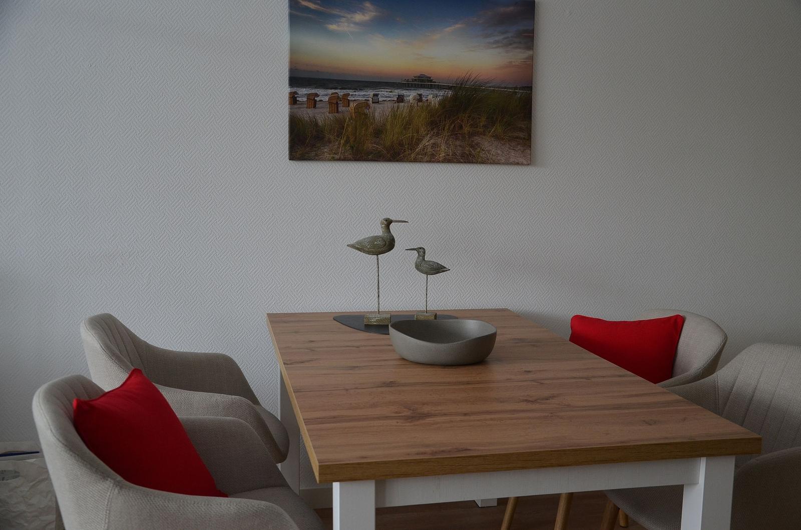 Esstisch mit Stühlen und roten Kissen, Wandbild und Vogeldekoration.