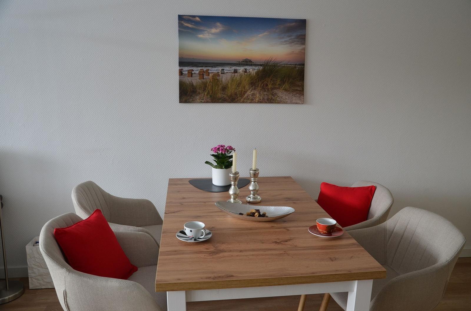 Esstisch mit vier Stühlen, roten Kissen und Wandbild am Hintergrund.