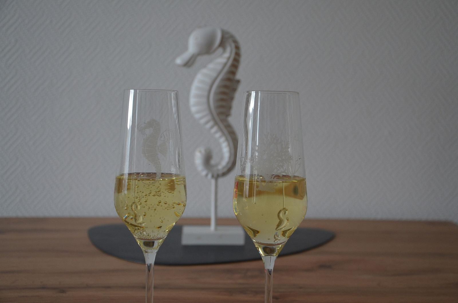 Zwei Gläser Sekt stehen auf einem Tisch neben einer Seepferdchen-Dekoration.