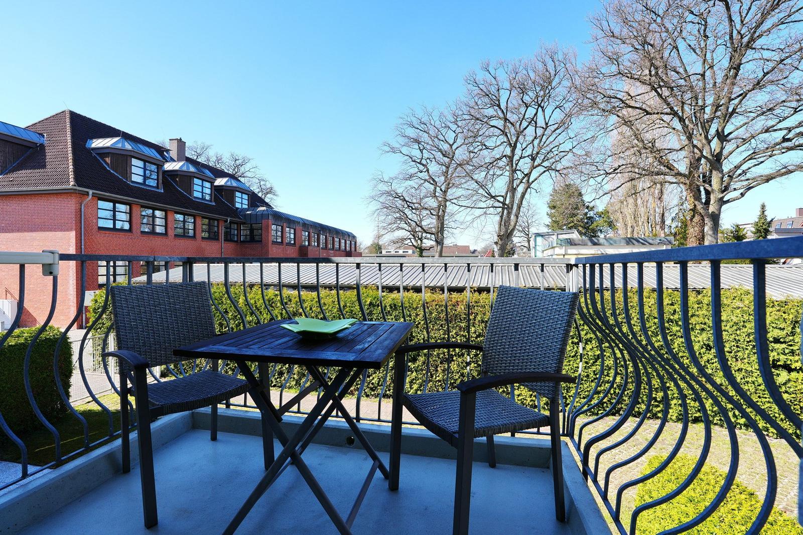 Terrasse mit Tisch und zwei Stühlen. Hintergrund: Gebäude und Bäume.