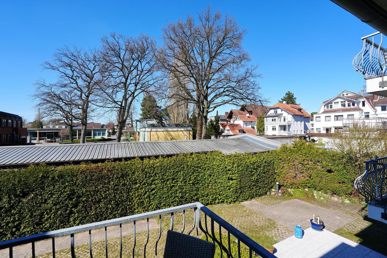 Terrasse mit Blick auf grüne Hecke und umliegende Häuser unter blauem Himmel.