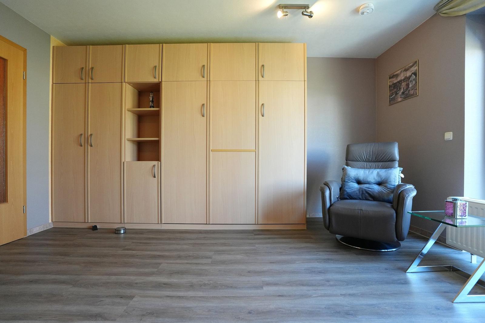 Großer Raum mit Holzschrank, Ledersessel und Glas-Tisch.