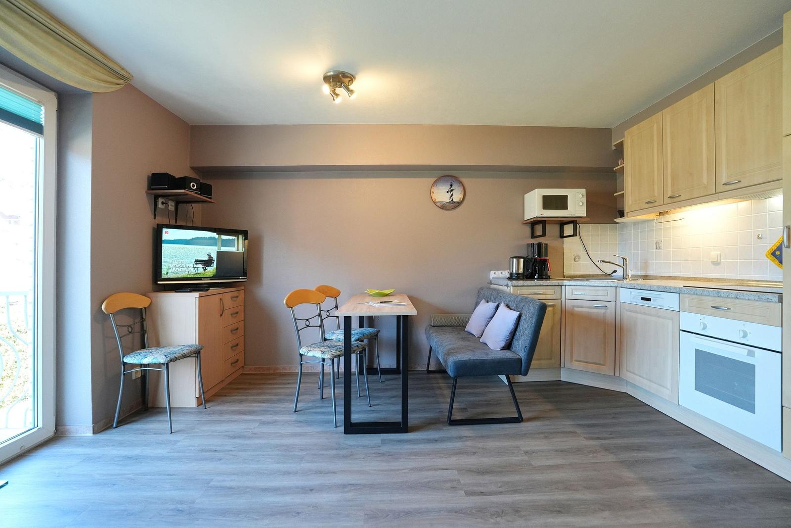 Küche mit Essbereich, Sofa, TV und Balkontür.