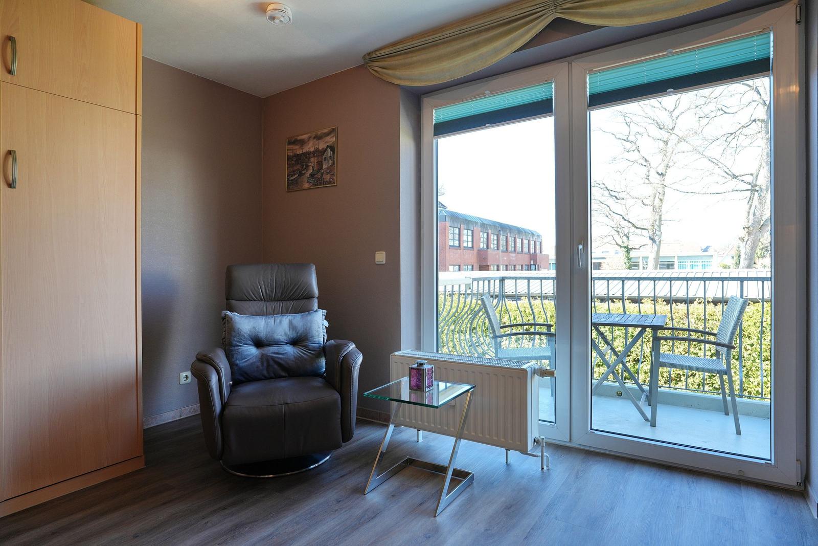 Zimmer mit Sessel, Schrank und Balkon mit Tisch und Stühlen.