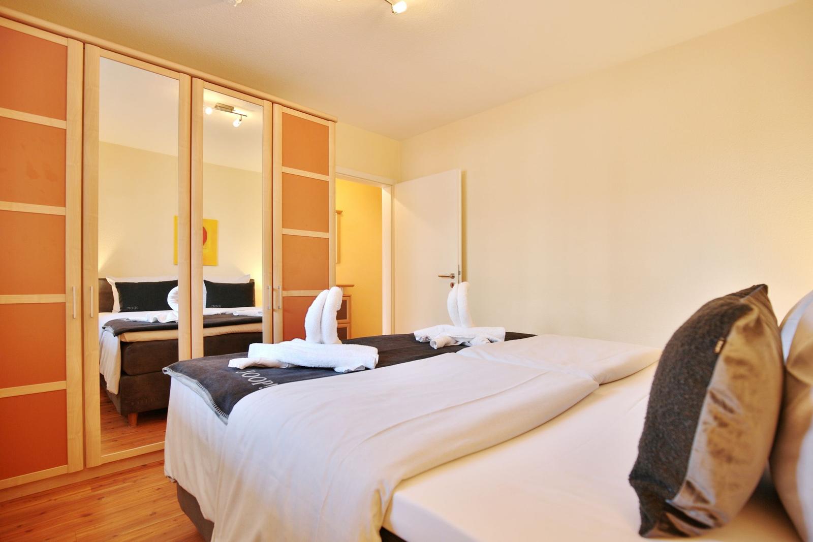 Schlafzimmer mit Bett, Spiegelschrank und Badetücher in Form von Schwänen.