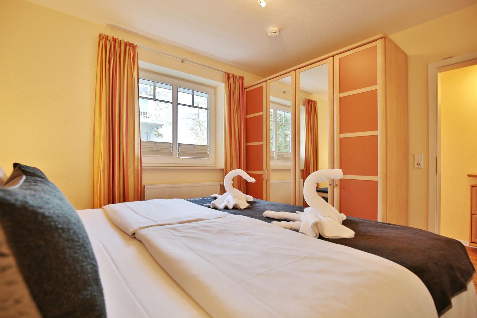 Schlafzimmer mit Bett, Fenster, Gardinen und Kleiderschrank mit Spiegeltüren.