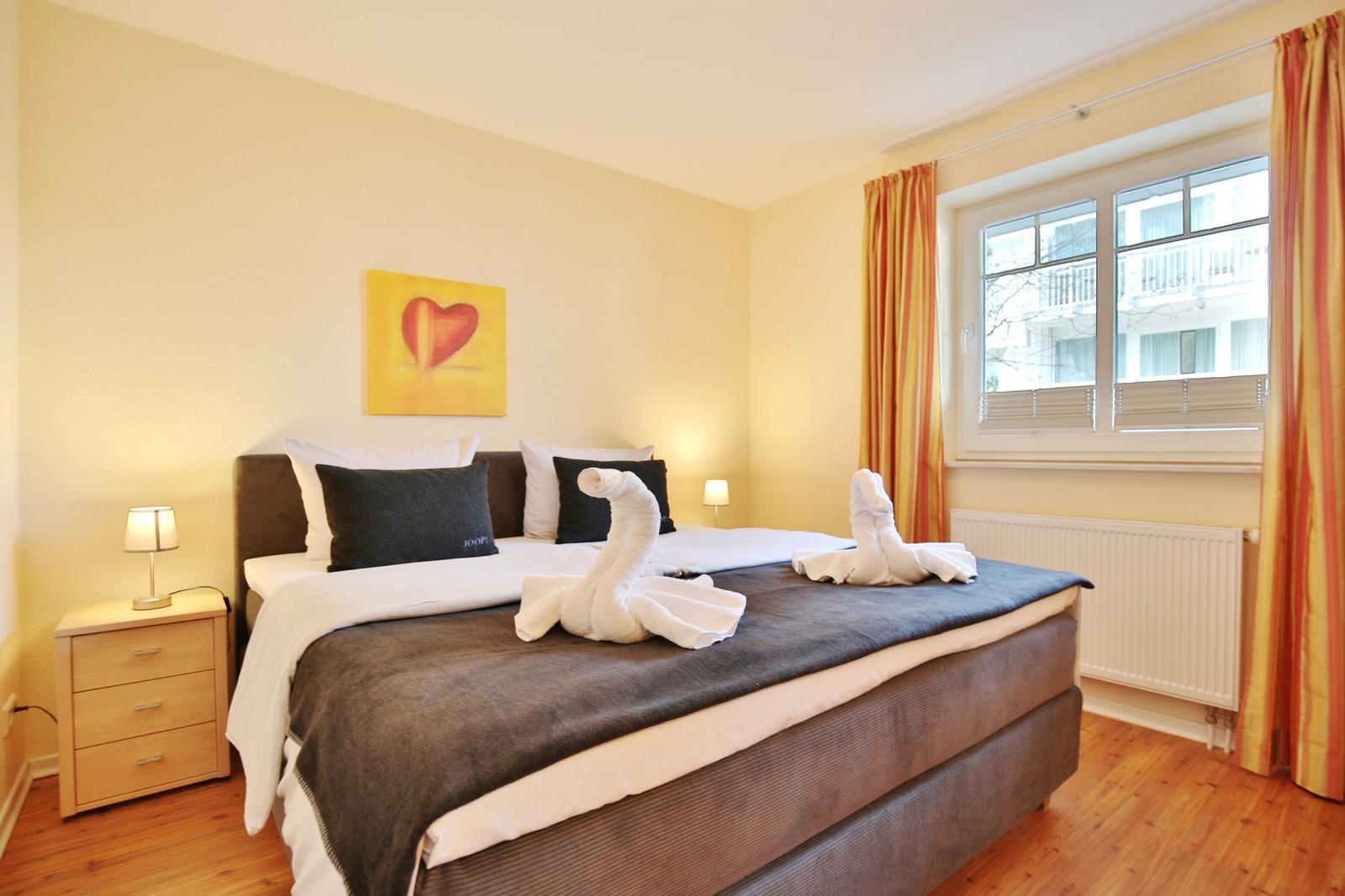 Schlafzimmer mit Bett, Nachttisch und Fenster mit Vorhängen.