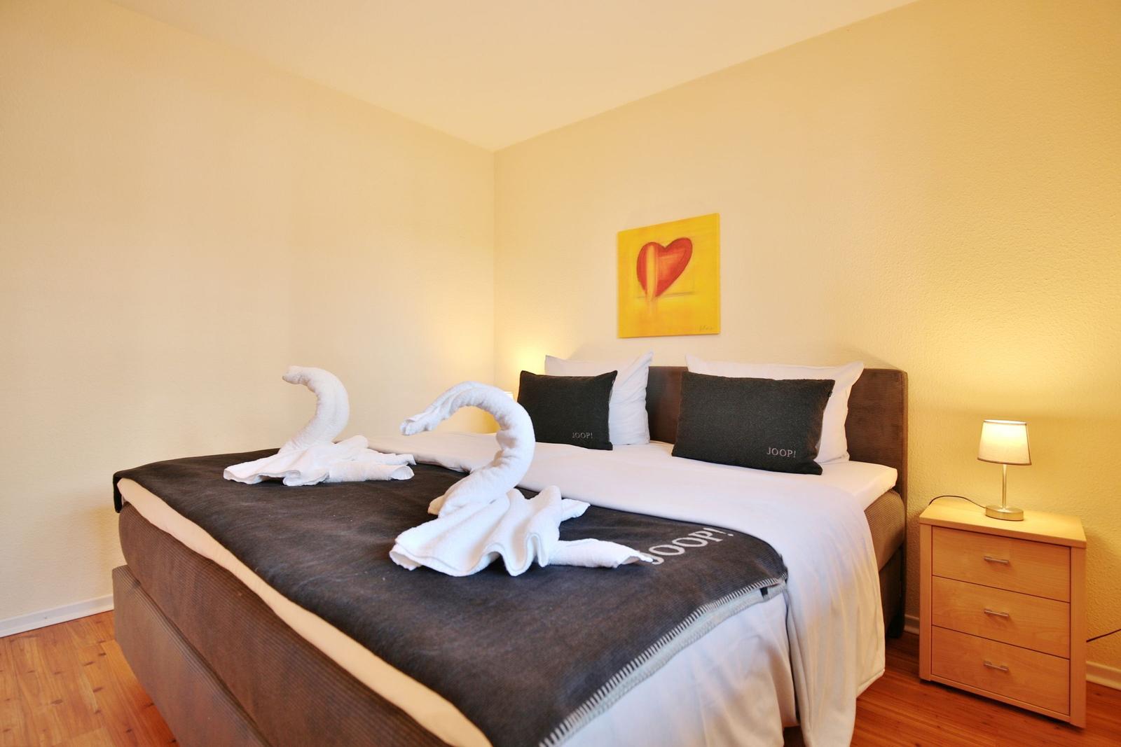 Schlafzimmer mit Bett, Nachttisch und Wandbild. Handtuchschwanen auf dem Bett.