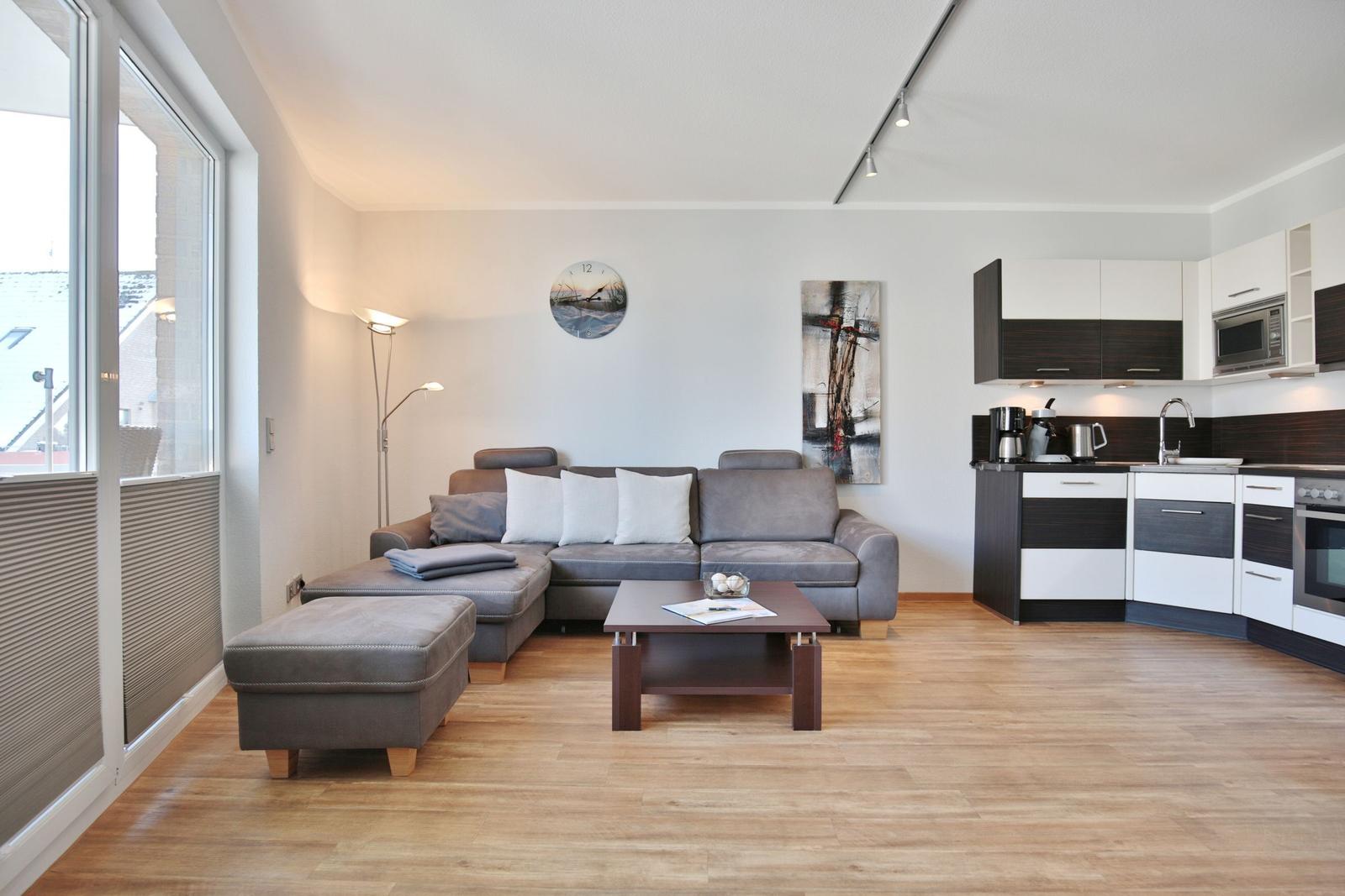 Wohnbereich mit Sofa, Couchtisch und Küche. Holzboden und große Fenster.