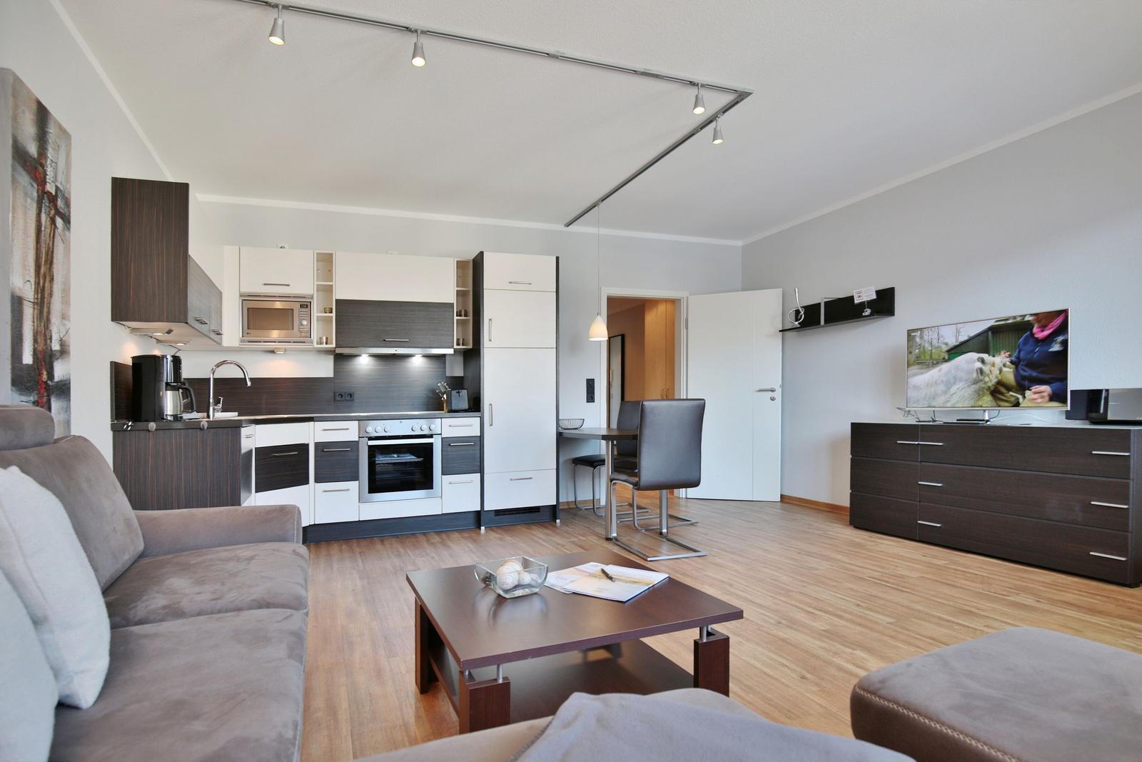 Wohnküche mit Sofa, TV und Esstisch. Holzboden und moderne Einrichtung.