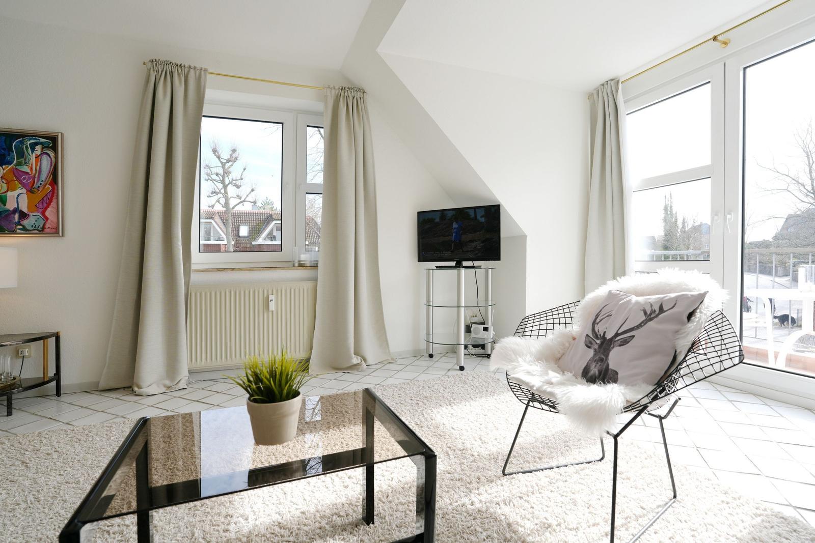 Wohnzimmer mit Fernseher, Sessel und Glas-Tisch. Fenster und Balkontür.