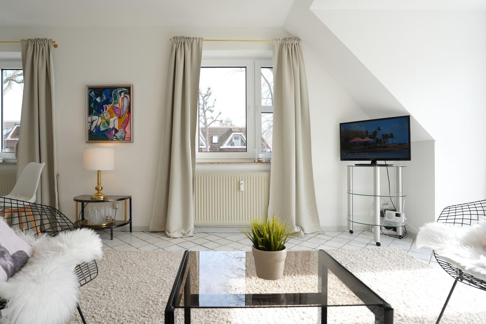 Wohnzimmer mit Glas-Tisch, zwei Stühlen und Fernseher an der Wand.