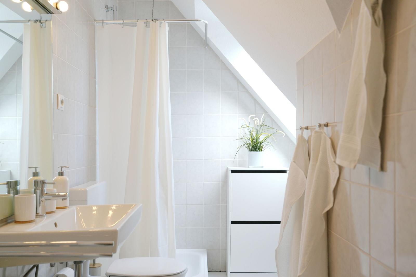 Badezimmer mit Dusche, Waschbecken und Toilette. Weiße Fliesen und Handtücher.