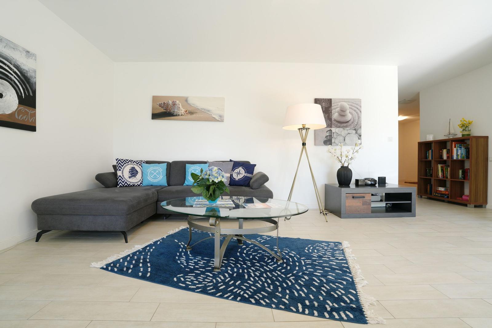 Wohnzimmer mit grauem Sofa, Glas-Tisch und blau-weißem Teppich