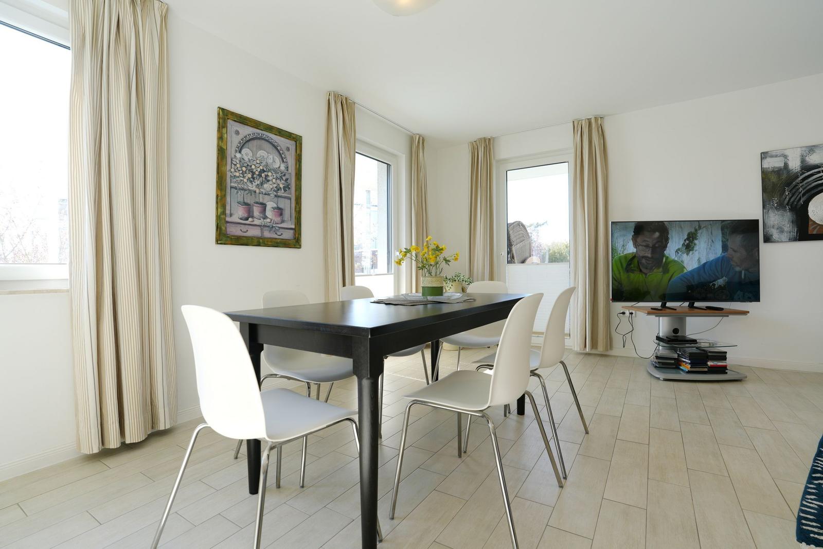 Esszimmer mit Tisch, Stühlen und TV. Fenster mit Vorhängen. Wandbilder.