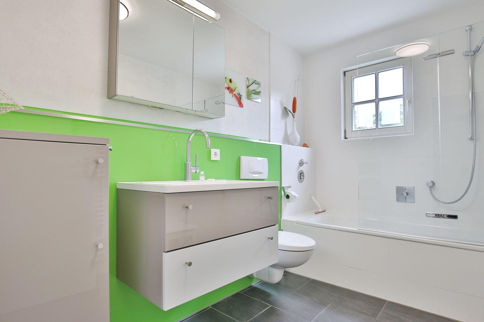 Bathroom with green accent, sink, shower, and window.