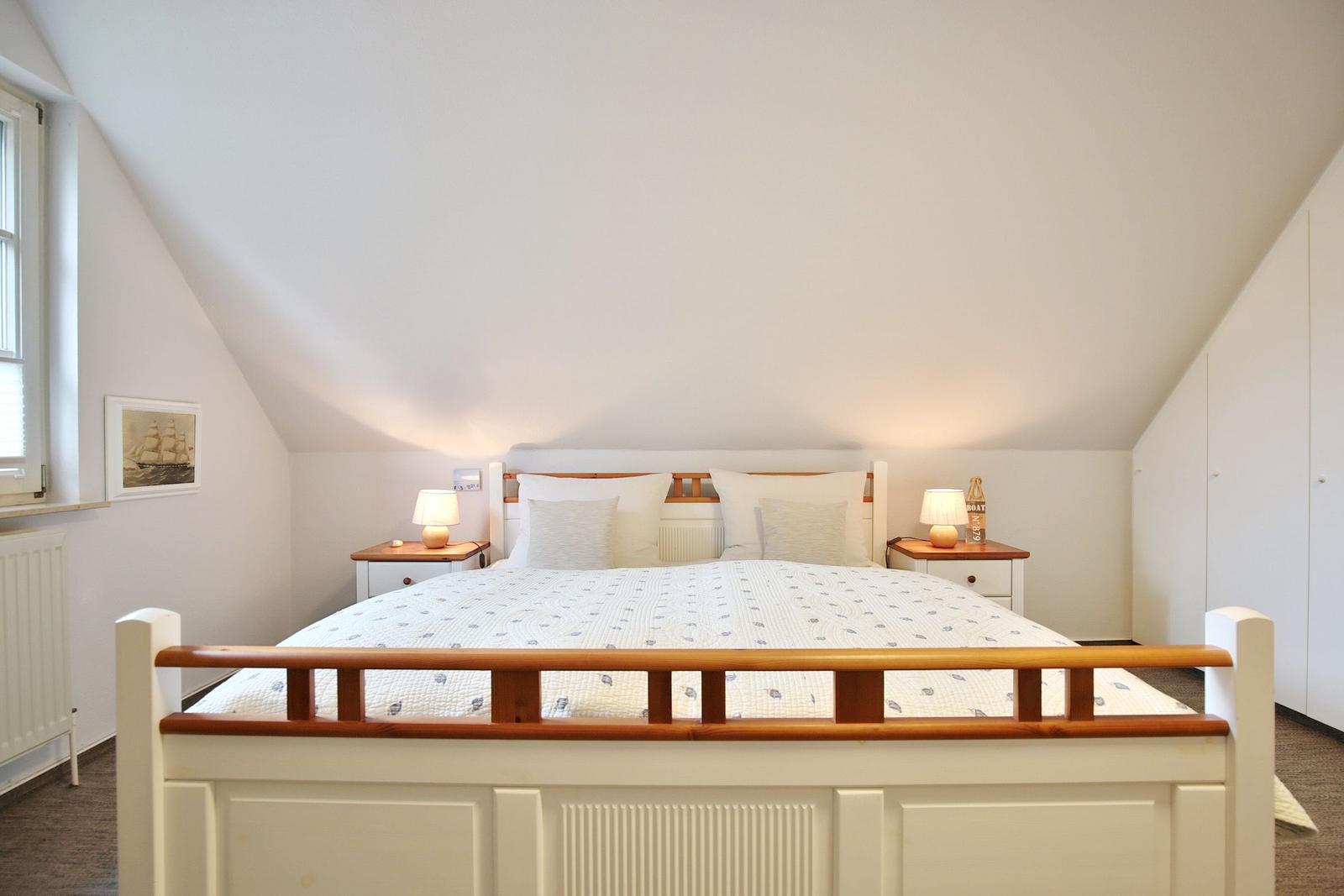 Bedroom with sloped ceiling, bed, nightstands, and window.